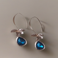 Lange goudkleurige oorbellen met bloemdetail en blauwe druppelhanger. Earrings by Tina