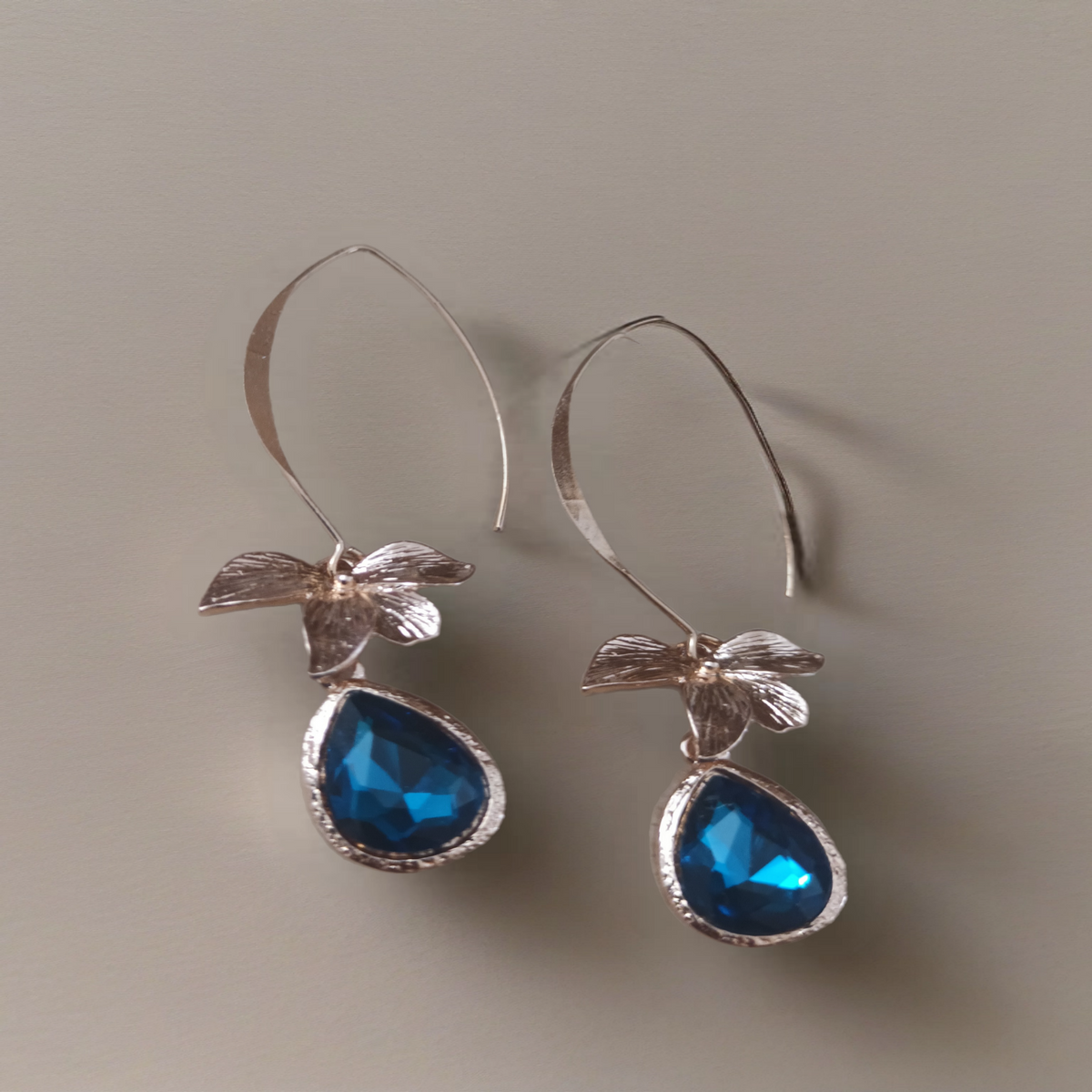 Lange goudkleurige oorbellen met bloemdetail en blauwe druppelhanger. Earrings by Tina