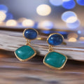 Blauw-turquoise hangende oorbellen met goudkleurige omlijsting. Earrings by Tina