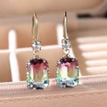Goudkleurige hangende oorbellen met rechthoekige transparante steen. Earrings by Tina