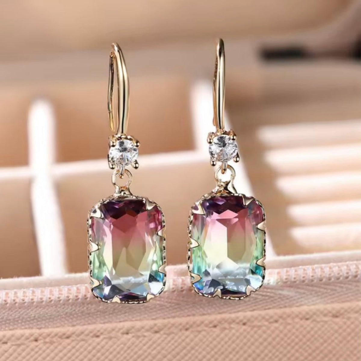 Goudkleurige hangende oorbellen met rechthoekige transparante steen. Earrings by Tina